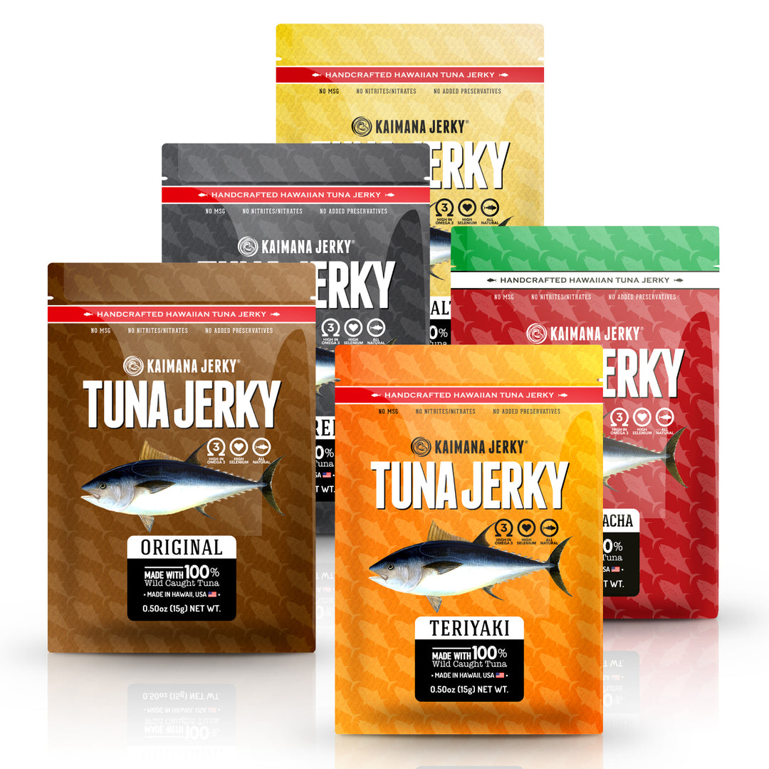 Six stand-up pouches of Kaimana Jerky Hawaiian Tuna Jerky displayed in a fan arrangement on a white background. The pouches are in different flavor colors: brown (Original), orange (Teriyaki), red (Sriracha),  grey (Peppered), and yellow (Lemon Salt).